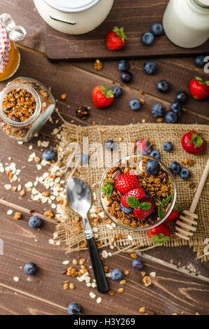 Joghurt mit gebackenem Müsli und Beeren in kleinen Glas, Erdbeeren, Heidelbeeren. Müsli mit Nüssen und Honig für kleine sw gebacken Stockfoto