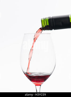 Rotwein aus der Flasche im Weinglas gießen. Isoliert auf weißem Hintergrund. Stockfoto