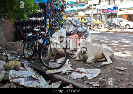 Männer sitzen in der Straße mit einer Heiligen Kuh in Dharavi Bezirk. Straßenszenen Mumbai, Indien Stockfoto