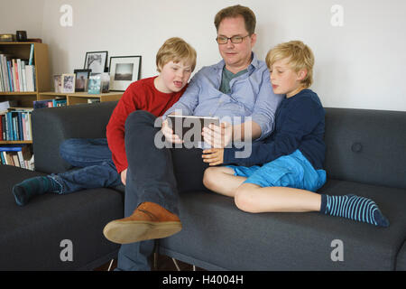 Vater und Söhne auf Sofa sitzend und mit digital-Tablette zu Hause Stockfoto