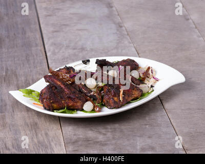 Jamaikanisches Jerk Chicken serviert auf einem Teller mit Holzhintergrund Stockfoto