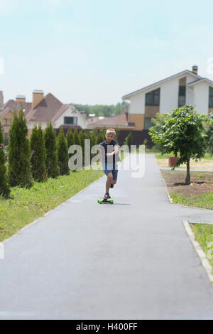 Junge Skateboard unterwegs inmitten von Bäumen gegen Häuser in der Stadt Stockfoto