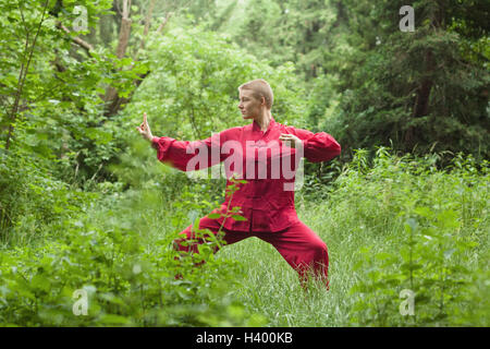 Frau Tai Chi üben, inmitten von Bäumen auf Feld konzentriert Stockfoto