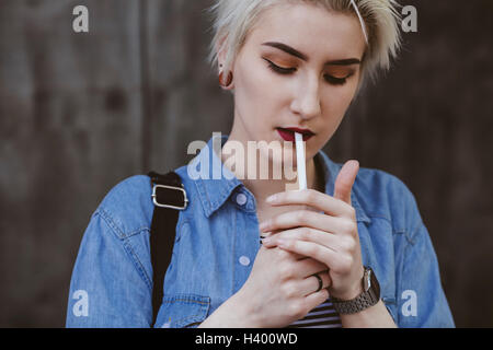 Junge modebewusste Frau Rauchen Zigarette im Freien stehen Stockfoto