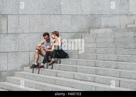 Glückliche Frau zeigt Smartphone Freund sitzend auf Schritte durch die Wand Stockfoto