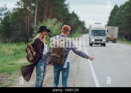 Glückliches Paar Trampen am Straßenrand im Wald Stockfoto