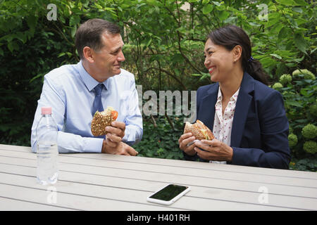 Glücklich Geschäftskollegen mit Snack am Tisch gegen Pflanzen Stockfoto