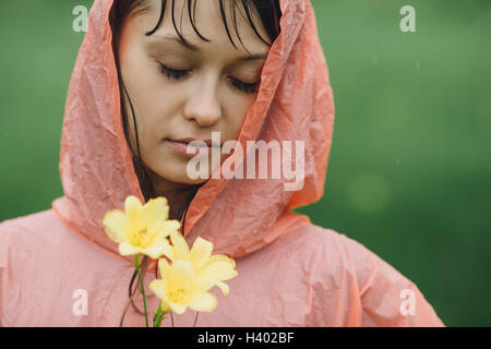 Schöne Frau mit Regenmantel mit gelben Blüten in Regenzeit in Nahaufnahme Stockfoto