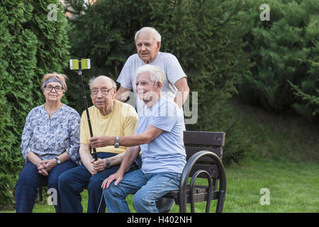 Lächelnden Senioren Freunde nehmen Selfie mit Einbeinstativ auf Parkbank Stockfoto