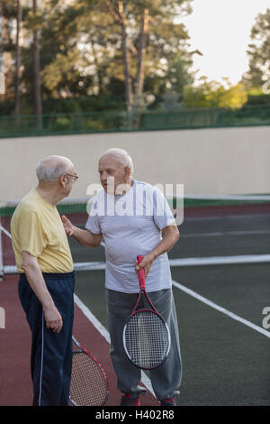 Senioren Freunde reden haltend Tennisschläger am Hof Stockfoto