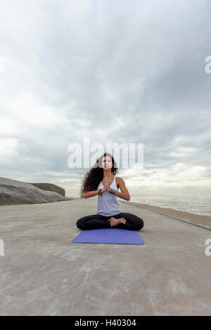 Junge Frau praktizieren Yoga im Gebet Position am Strand gegen bewölktem Himmel Stockfoto
