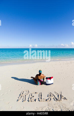 Frau sitzt am Strand mit Wort entspannen Sie sich im Sand, Türken und Caicos, Karibik Stockfoto