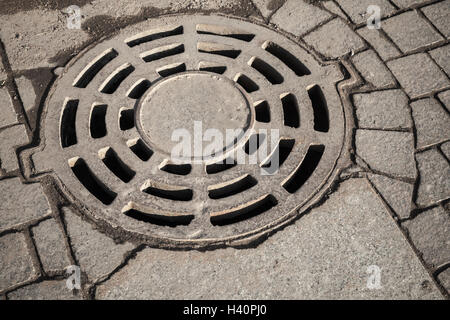 Alte Runde Kanalisation Kanaldeckel in graue Kopfsteinpflaster Straßenpflaster Stockfoto