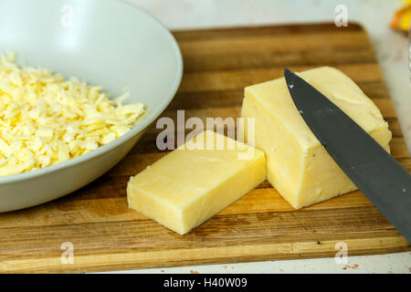 Block von Cheddar-Käse auf einem Holzbrett, teilweise zerkleinert Stockfoto