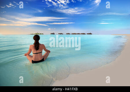 Junge Frau, die Ausübung von Yoga in der türkisfarbenen Lagune mit Wasserbungalows auf tropischen Insel Stockfoto