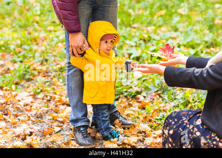 Vater, Mutter und Sohn zu Fuß. Baby, die ersten Schritte mit Hilfe des Vaters im Herbst Garten in der Stadt Stockfoto