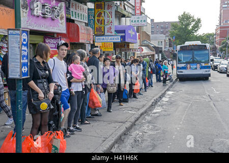 Ein gemischtes Publikum von Menschen warten auf ein City-Bus in der Innenstadt von Flushing, Queens, New York City. Stockfoto