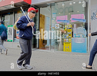 Eine ältere asiatisch-amerikanische mit seinem Stock, Lebensmittel zu tragen und nicht zu helfen, zu Fuß in Chinatown, Downtown Flushing Queens, NYC Stockfoto