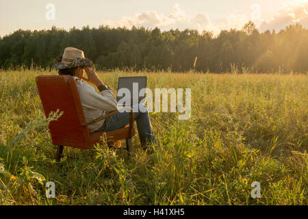 Mari Mann sitzend auf Stuhl im Feld mit laptop Stockfoto