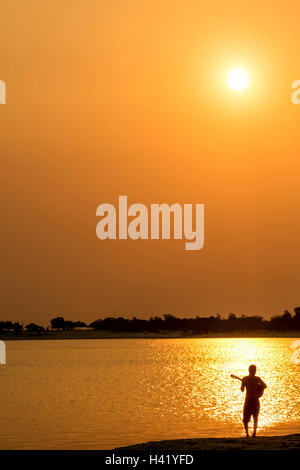 Silhouette des kaukasischen Mann Gitarre am Strand bei Sonnenuntergang Stockfoto