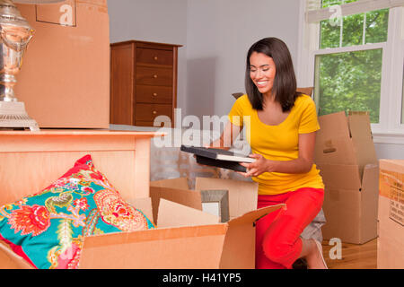 Hispanic Frau kniet am Boden packen Bücher in Umzugskartons Stockfoto