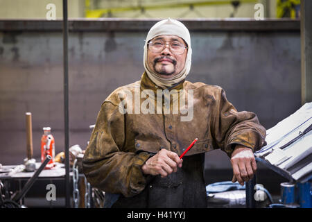 Lächelnde asiatische Arbeiter Haube posiert in Fabrik Stockfoto
