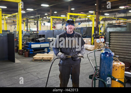 Kaukasische Schweißer posiert mit Lötlampe in Fabrik Stockfoto