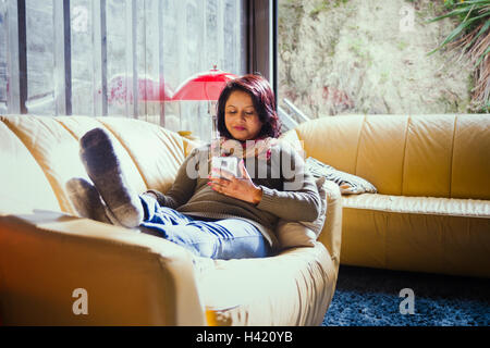 Frau sitzt auf dem Sofa SMS auf Handy Stockfoto