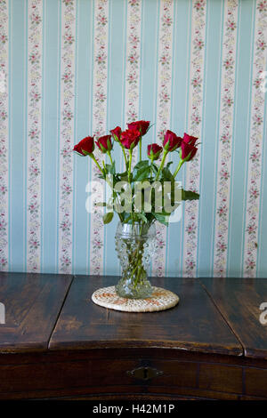 Rote Rosen in Vase auf Sideboard mit floral Tapete im Hintergrund Stockfoto