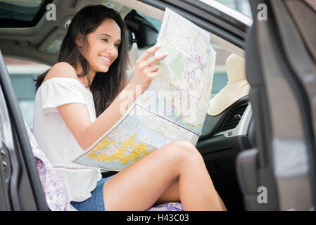 Gemischte Rennen Frau sitzt im Auto lesen Karte Stockfoto