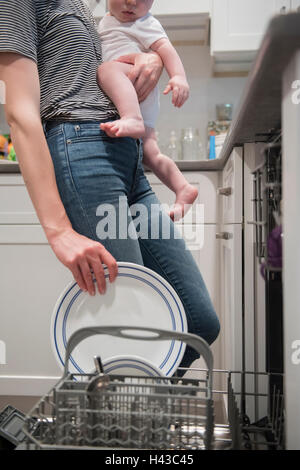 Kaukasische Mutter hält Baby Sohn Halteblech in Spülmaschine Stockfoto