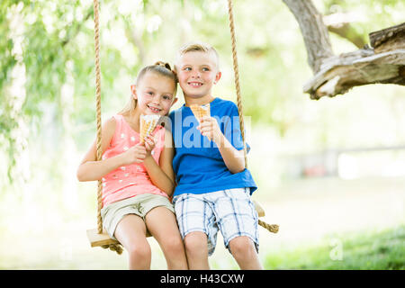 Kaukasische Bruder und Schwester essen Eis Creme Kegel auf Seil Schaukeln Stockfoto