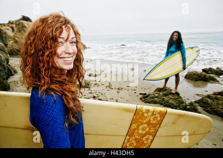 Lächelnde Frauen Surfbretter am Strand Stockfoto