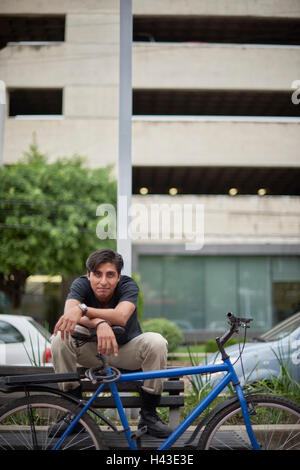 Lächelnder Hispanic Mann sitzen auf Bank mit Fahrrad Stockfoto