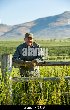 Kaukasische Landwirt mit Handschuhen stützte sich auf Holzzaun Stockfoto