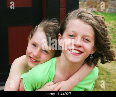 Zwei glückliche junge Mädchen oder Geschwister, Schwestern für die Kamera posieren, Huckepack Fahrt Stockfoto