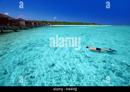 Junger Mann Schnorcheln in tropischen Insel mit Sandstrand, Palmen, Wasserbungalows und Türkis klarem Wasser Stockfoto