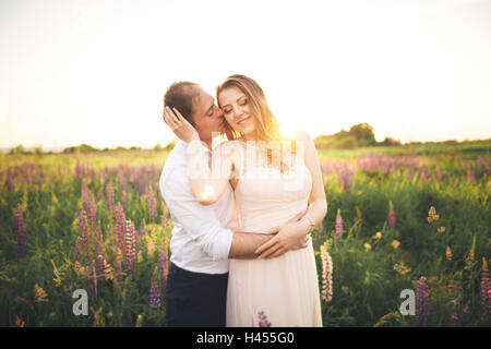 Braut hält Bräutigam Hals, während er ihr in den Strahlen des Sonnenuntergangs küsst Stockfoto
