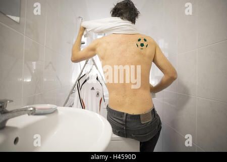 Badezimmer, Mann, Badewanne Rand, sitzt, obere Körper frei, Schulterblatt, Tattoo, "Fußball", keinen Besitz loslassen, Mann, jung, Rücken, Tätowierungen, Fußball-Fan, Ventilator, Hintergrund, Kleiderständer, Fußballtrikot, Trikot, reinigt trocken, Fan-Artikel-Begeisterung "mit Leib und Seele", symbol, Fußball, Fußball Spiele, WM, Fußball-WM, Bundesliga, Interieur, Stockfoto