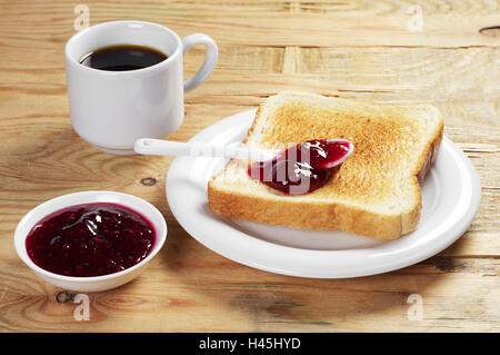 Toast mit Himbeermarmelade und Tasse heißen Kaffee auf alten Holztisch Stockfoto