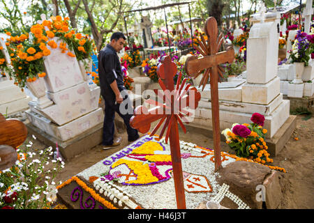 Ein Mann geht vorbei an Grabstätten, verziert mit aufwendigen floralen Pedal Wandteppiche zu Ehren des Verstorbenen auf dem Friedhof San Antonino Castillo im Laufe des Tages von den Dead Festival bekannt als D'a de Muertos am 3. November 2013 in San Antonino Castillo Velasco, Oaxaca, Mexiko. Stockfoto