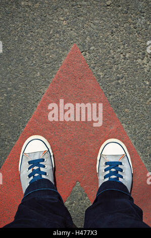Sneakers auf der Asphaltstraße mit rot gezeichnete Richtungspfeil. Stockfoto