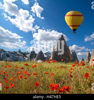 Heißluftballons fliegt über ein Feld von Mohn und Felslandschaft in Kappadokien, Türkei Stockfoto