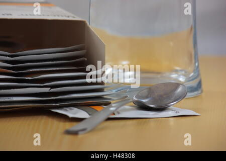 Ein Tisch mit einer Medizin und ein Glas Wasser umgeben von Kisten mit einem verschreibungspflichtigen Medikamenten. Stockfoto