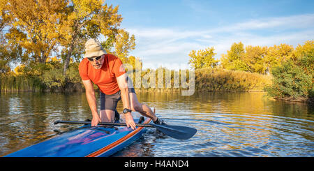 Senior männlichen Paddler startet Training auf seinem Renn-Stand up Paddleboard in Herbstfarben auf See in Colorado Stockfoto