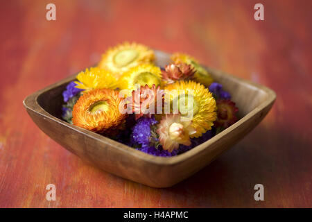 Gelbe und rote Streublumen in hölzernen Schale am roten Tisch, Stockfoto