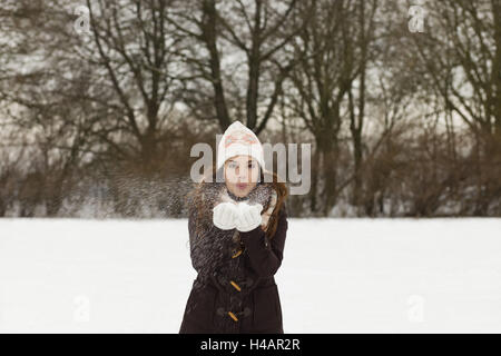 junge Frau bläst Schnee aus ihren Handflächen, gerichtete Kamera, halbe Portrait, Stockfoto