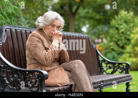 Traurig ältere Frau sitzen auf einer Bank im Herbst park Stockfoto