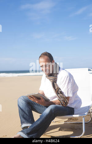 Mann nutzt seine Tablet-PC am Strand, Stockfoto