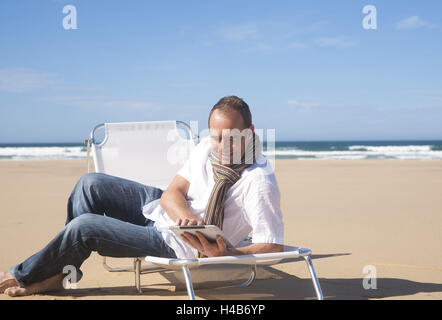 Mann nutzt seine Tablet-PC am Strand, Stockfoto